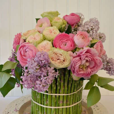 Pink and lavender flowers arranged in a vase wrapped with asparagus spears