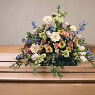 Floral arrangement on a casket with pastel flowers and blue accents