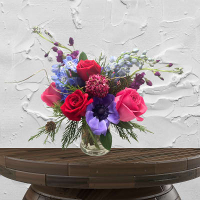 Mixed bouquet of roses and purple flowers in a clear glass vase