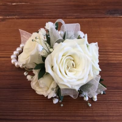 Wrist corsage of white roses and small white blooms on a pearl bracelet