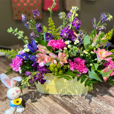 Mixed bouquet in a pale yellow basket with a small bunny figurine beside it