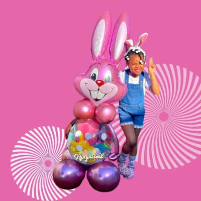 Girl posing beside a pink bunny balloon sculpture on a pink background