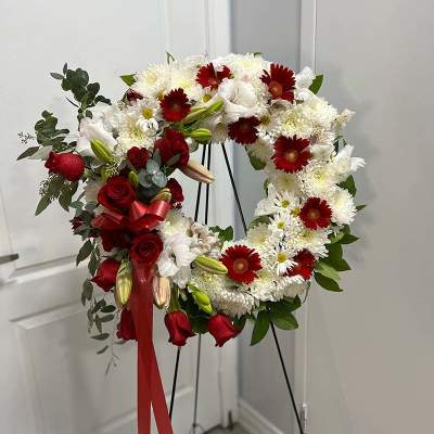 Red and white floral wreath on a black stand with a red ribbon
