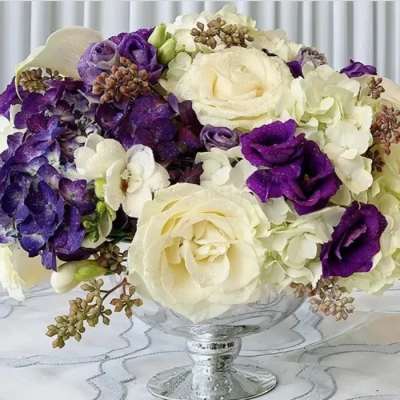Purple and white floral bouquet in a clear glass pedestal vase
