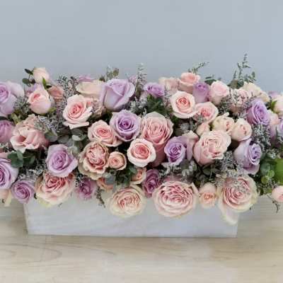 Low rectangular arrangement of pink and lavender roses in a white container