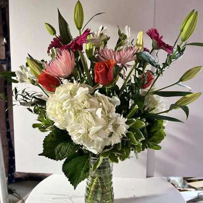 Mixed bouquet in a glass vase with lilies, roses, hydrangea, and pink daisies