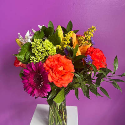 Mixed bouquet in a clear glass vase with orange, purple, and green blooms
