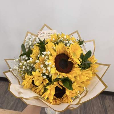 Hand-tied bouquet of bright yellow sunflowers and tiny white blooms wrapped in cream and gold paper