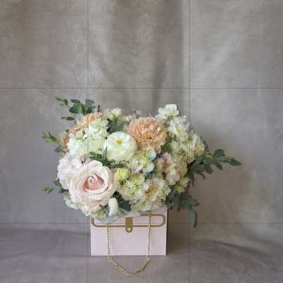 Pastel flower arrangement in a pink gift box with a gold chain handle