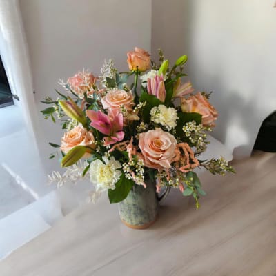 Peach roses and pink lilies arranged in a ceramic pitcher vase
