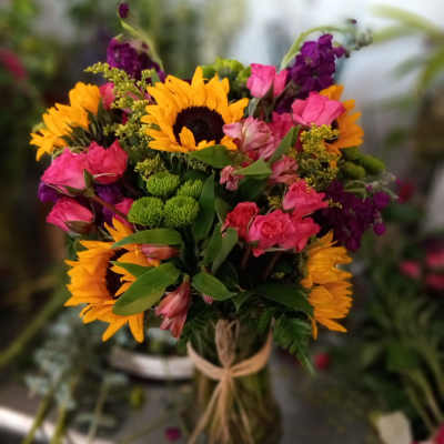 Mixed bouquet with sunflowers, pink roses, and purple flowers in a glass vase