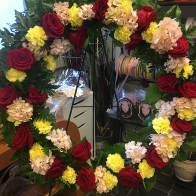 Large floral wreath with red roses, yellow carnations, and pale hydrangeas
