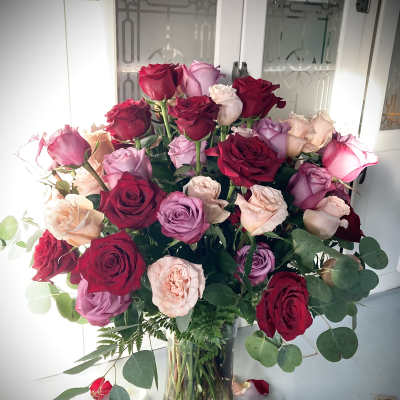 Bouquet of red, pink, and lavender roses in a clear glass vase