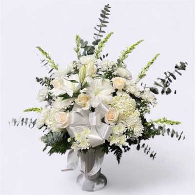 White floral arrangement in a silver vase with a large white ribbon