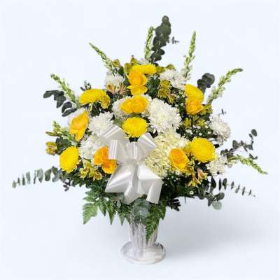 Yellow and white floral arrangement in a silver vase with a white bow