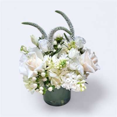White floral arrangement in a green glass vase with tall curved stems