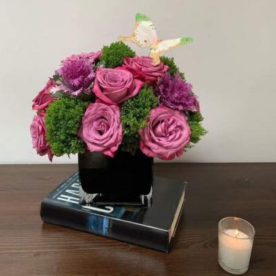 Pink roses in a black vase with a small butterfly topper