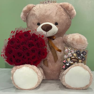 Large teddy bear holding red roses and a box of chocolates