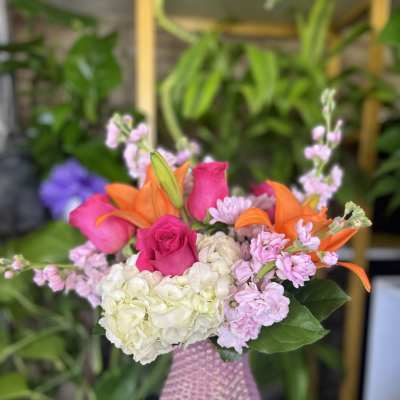 Pink roses and orange lilies arranged with hydrangea in a pink vase