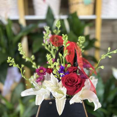 Small floral arrangement with red roses and white lilies in a black container