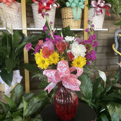 Mixed bouquet in a red glass vase with a pink ribbon bow