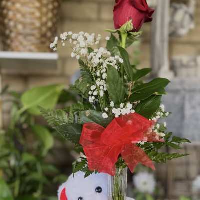 Single red rose in a glass vase with a teddy bear and heart decoration