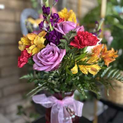 Colorful bouquet of roses, carnations, and alstroemeria in a red vase with a pink ribbon