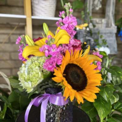 Bouquet with a sunflower, pink blooms, and yellow lilies in a dark vase