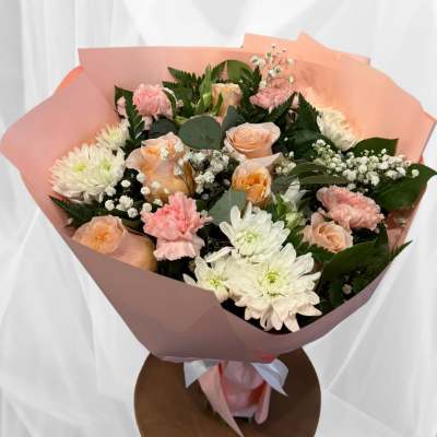 Bouquet of peach roses, pink carnations, and white chrysanthemums wrapped in pink paper