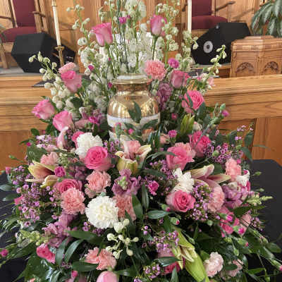 Large pink and white floral funeral arrangement with a gold urn centerpiece