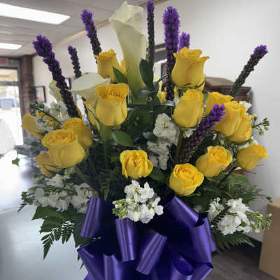 Yellow roses and white calla lilies in a glass vase with purple ribbon