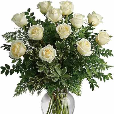 White roses arranged in a clear glass vase with dense greenery