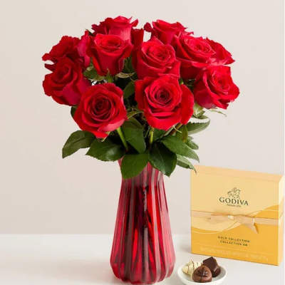 Red roses in a red glass vase with a box of chocolates beside them