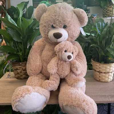 Two plush teddy bears sit among potted plants under a lit "FLOWERS" sign.