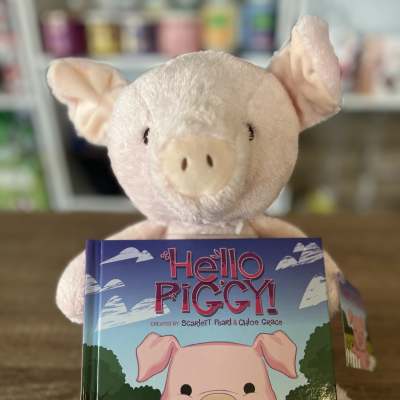 Plush pig holding a children's book titled Hello Piggy