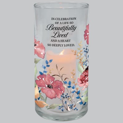 Glass cylinder candle holder with pink floral design and memorial quote around a lit pillar candle.