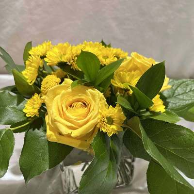 Yellow roses and small yellow daisies in a clear glass vase