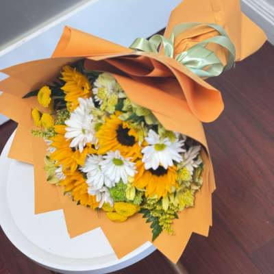 Bouquet of yellow sunflowers and white daisies wrapped in orange paper