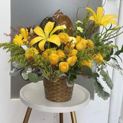 Yellow lilies and roses arranged in a woven basket