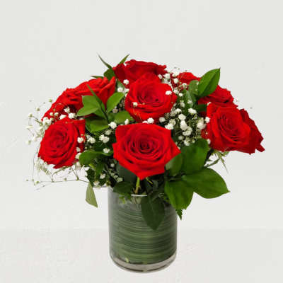 Red roses arranged in a glass vase with baby's breath and greenery