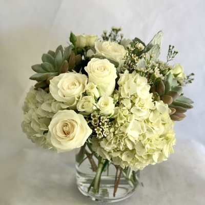 Cream roses and hydrangeas arranged in a clear glass vase