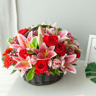 Basket arrangement of pink lilies and red roses