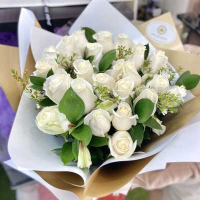 Handheld bouquet of white roses with green accents wrapped in layered white and tan paper