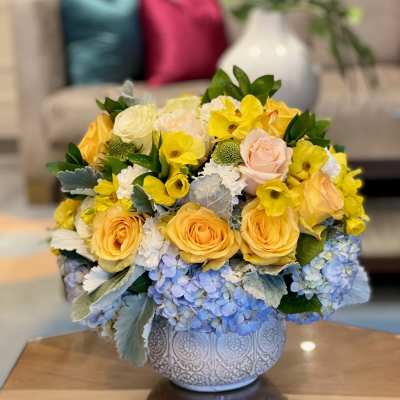 Yellow and peach roses with blue hydrangeas in a patterned vase