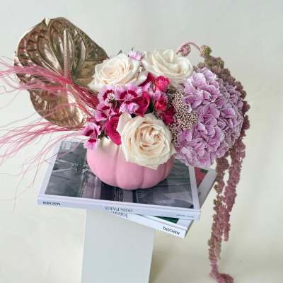 Pink and white floral arrangement in a pumpkin vase with a metallic leaf accent