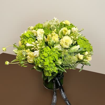 Green and white floral arrangement in a dark vase with ribbon