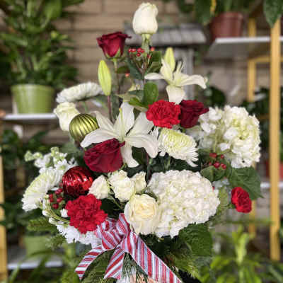 Red and white floral arrangement in a white vase with a striped ribbon