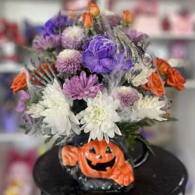 Halloween bouquet with purple, white, and orange flowers in a pumpkin base