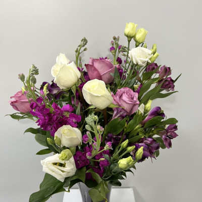 Mixed bouquet of pink, white, and purple flowers in a dark vase