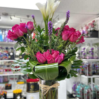 Tall arrangement of hot pink roses and white calla lilies in a clear glass vase with a collar of broad green leaves